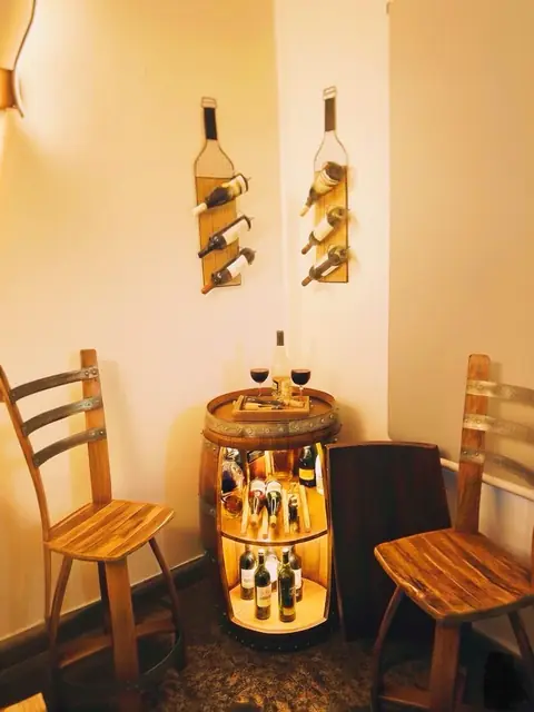 A corner fitted out with two wall racks and an illuminated barrel bar between two chairs.