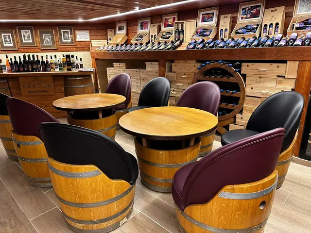 Barrel armchairs in burgundy and black around round oak tables in a winery tasting room.
